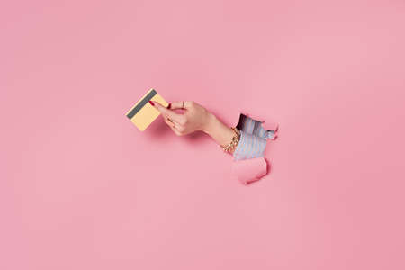 Partial view of credit card in hand of woman near pink background with hole