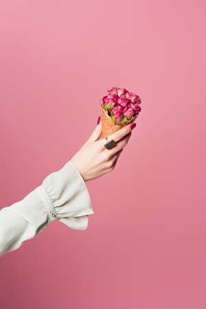 Cropped view of woman holding waffle cone with blooming flowers isolated on pinkの写真素材