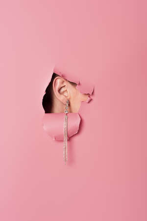 Cropped view of woman in earring near pink background with holeの写真素材