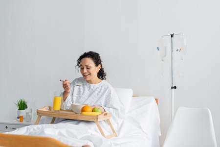 happy african american woman having breakfast near fresh fruits and orange juice in hospitalの写真素材