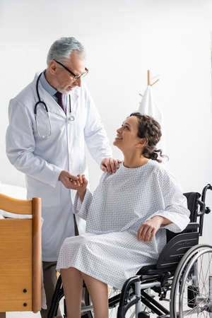 mature doctor holding hand of smiling african american woman sitting in wheelchairの写真素材
