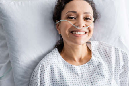 top view of smiling african american woman with nasal cannula lying in hospital bedの写真素材