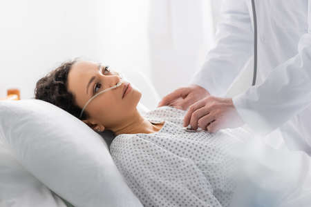 doctor examining diseased african american woman with stethoscope on blurred foreground