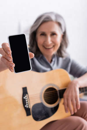 blurred and happy mature woman with gray hair holding smartphone with blank screen and acoustic...