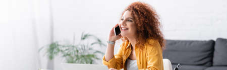 joyful freelancer with curly hair talking on cellphone at home, banner