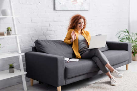 happy woman waving hand during video call on laptop at homeの写真素材