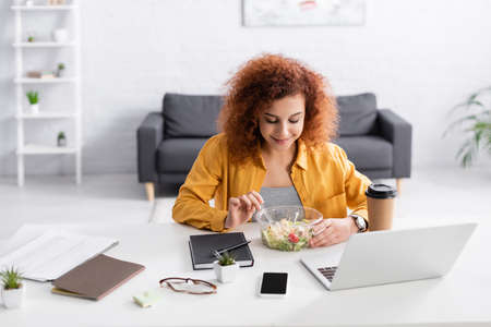 young freelancer eating fresh salad near laptop at homeの写真素材