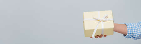 cropped view of woman holding gift box with white ribbon isolated on gray, banner