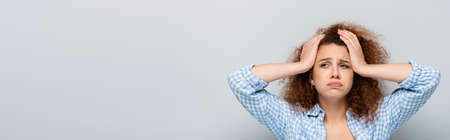 exhausted woman with curly hair holding hands on head on gray background, bannerの写真素材