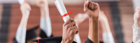 Cropped view of multiethnic students holding diploma near hands of blurred friends, banner