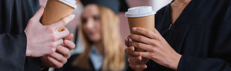 Cropped view of interracial graduates holding coffee to go, bannerの写真素材