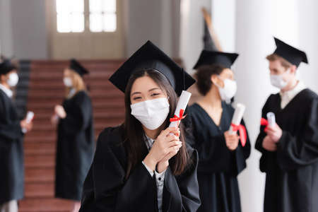 Asian bachelor in protective mask holding diploma in universityの写真素材
