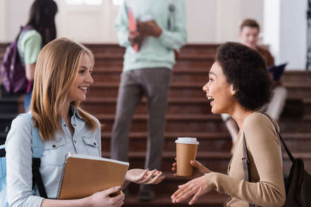 Positive interracial students with notebook and coffee talking