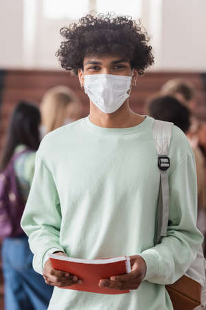 African american student in medical mask holding notebook