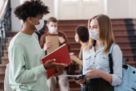 Interracial students in medical masks holding notebooks and talkingの写真素材