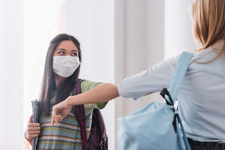 Asian student in medical mask doing elbow bump with friends in university