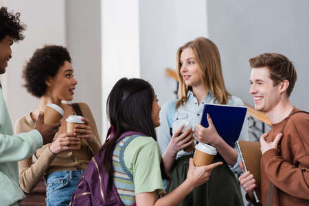 Positive multicultural students with paper cups talking in hall