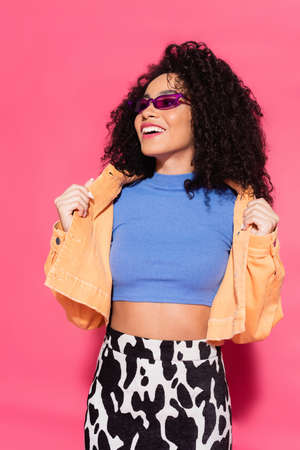cheerful african american woman in sunglasses posing on pink