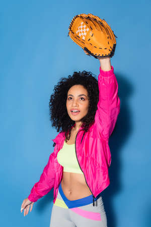 sporty african american woman in leather glove playing baseball on blueの写真素材
