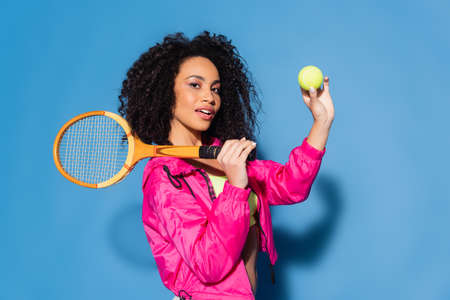 curly african american woman holding tennis racket and ball on blueの写真素材