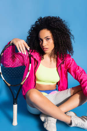 african american woman holding tennis racket and sitting on blueの写真素材