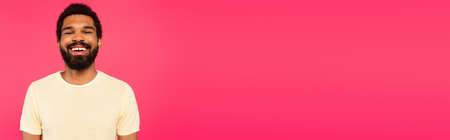 cheerful and bearded african american man smiling isolated on pink, banner