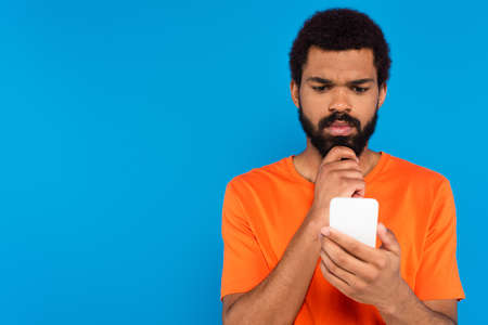 thoughtful african american man using smartphone isolated on blue
