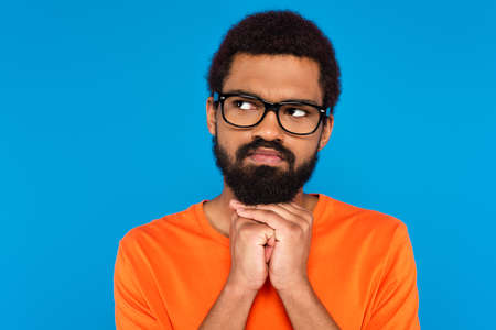 thoughtful african american man in glasses looking away isolated on blue