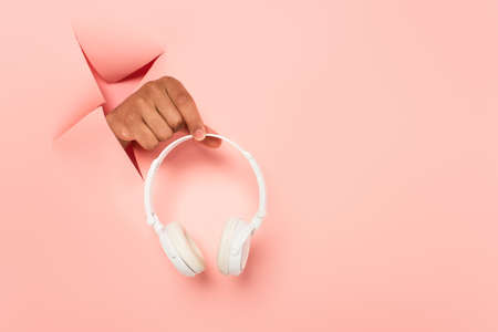 partial view of african american man holding wireless headphones on ripped pink backgroundの写真素材