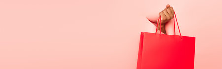 partial view of african american man holding shopping bag on ripped pink background, bannerの写真素材