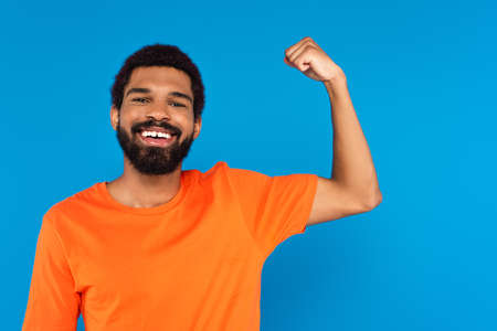 bearded african american man smiling and showing muscle isolated on blue