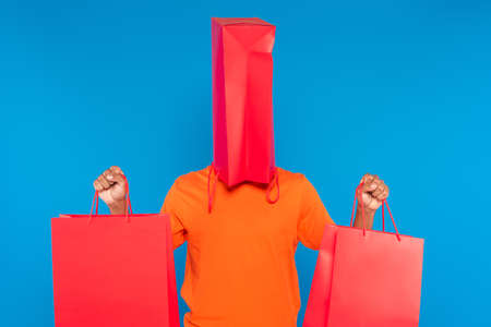 african american man with shopping bag on head holding paper bags with purchases isolated on blue