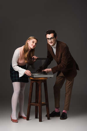 full length view of happy couple in retro outfit near record player on dark gray background