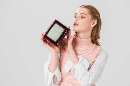 dreamy, retro style woman holding vintage tv while looking away isolated on grayの写真素材