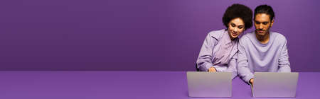 cheerful african american freelancers using laptops isolated on purple, bannerの写真素材