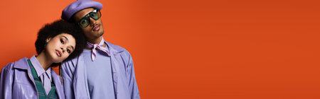 stylish woman in purple jacket leaning on man in beret and sunglasses isolated on orange, bannerの写真素材