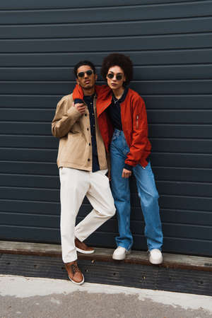 full length of young african american woman posing with stylish man in sunglasses outside