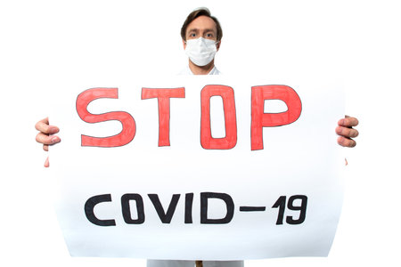 Placard with stop covid-2019 lettering in hands of blurred doctor in medical mask isolated on whiteの写真素材