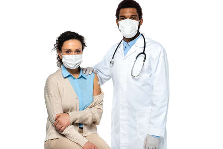 African american doctor in latex gloves standing near patient in medical mask and adhesive patch on arm isolated on whiteの写真素材