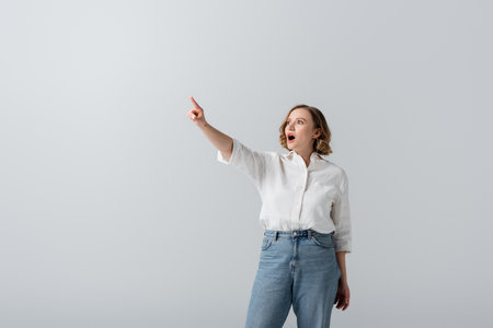 overweight and shocked woman in white shirt pointing with finger isolated on grayの写真素材