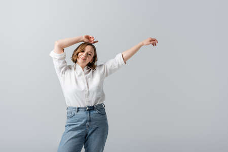overweight and pleased woman in white shirt posing with hands above head isolated on grayの写真素材