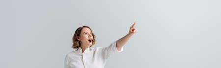 overweight and shocked woman in white shirt pointing with finger isolated on gray, bannerの写真素材