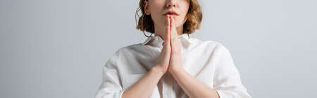 cropped view of young overweight woman in white shirt with praying hands isolated on gray, banner