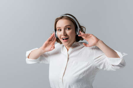 amazed plus size woman in wireless headphones listening music isolated on grayの写真素材
