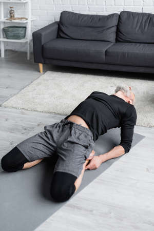 bearded man in sportswear stretching on fitness mat in living room