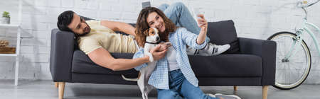 happy young woman taking selfie with jack russell terrier and muslim boyfriend, banner