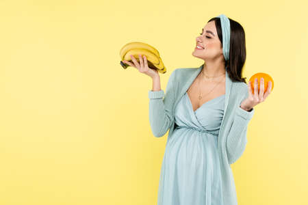 joyful pregnant woman holding ripe bananas isolated on yellowの写真素材