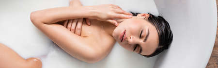 young woman touching neck and covering breast with hand in milk bath, bannerの写真素材