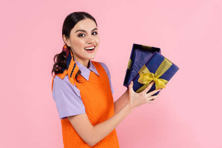 amazed woman holding presents and looking at camera isolated on pinkの写真素材
