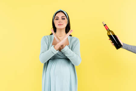 pregnant woman showing stop gesture near bottle of red wine isolated on yellowの写真素材